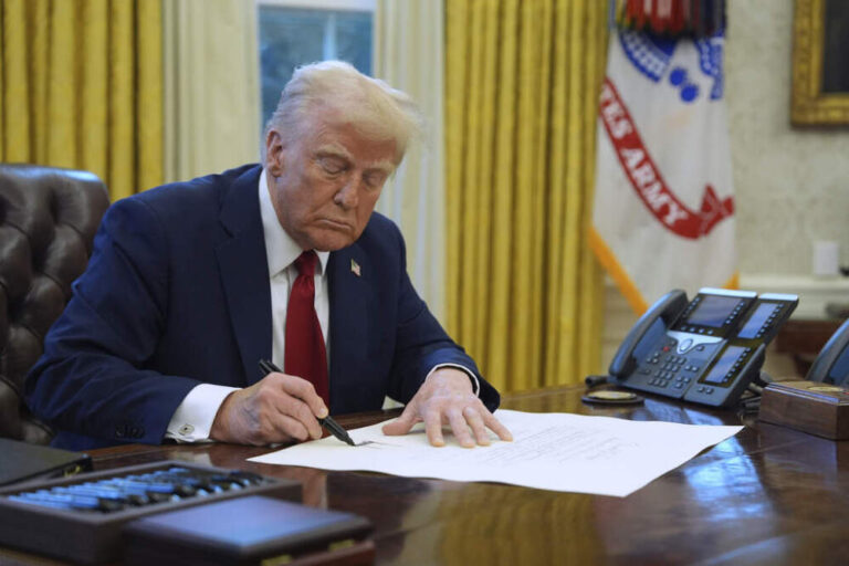 President Donald Trump signing a bill at his desk in the Oval Office, focused on the document in front of him.